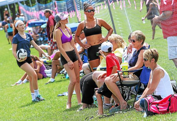 Group of volleyball players and spectators standing and sitting in the grass.