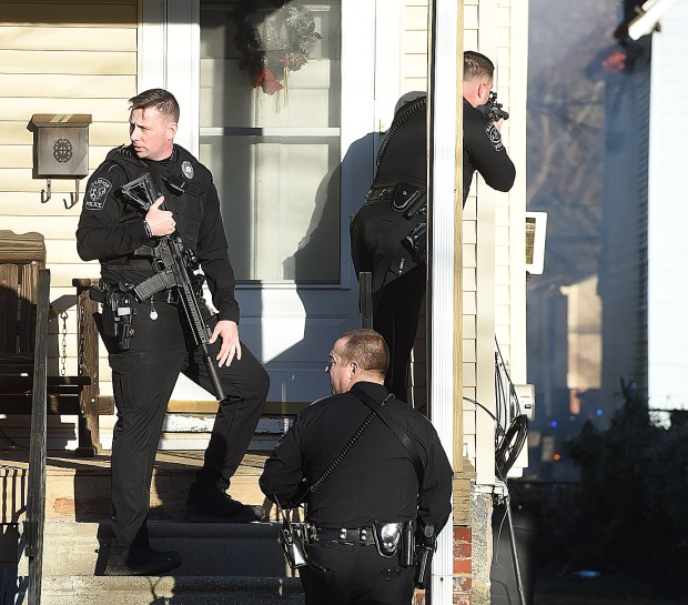 3 police officers, two with long guns, approach the front door to a home