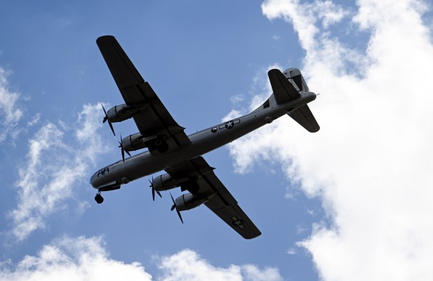 Vintage WWII airplane flying with blue sky and clouds.